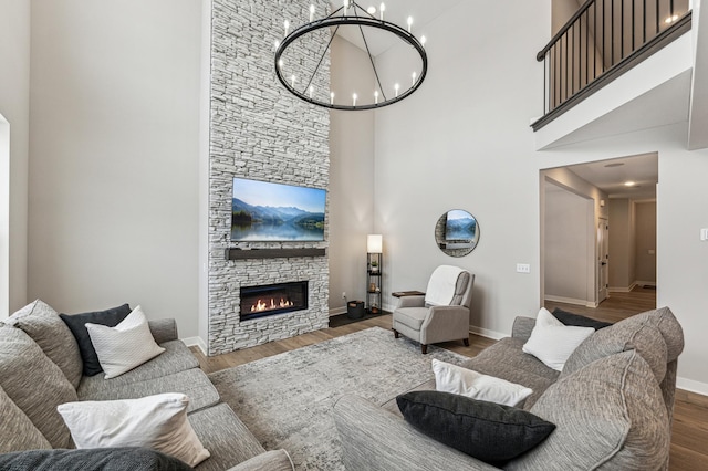 living room featuring an inviting chandelier, a stone fireplace, dark hardwood / wood-style floors, and a high ceiling