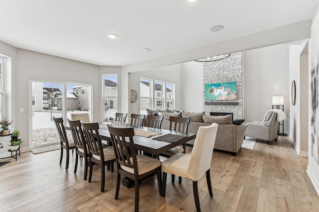 dining area featuring a stone fireplace, a healthy amount of sunlight, a chandelier, and light hardwood / wood-style floors