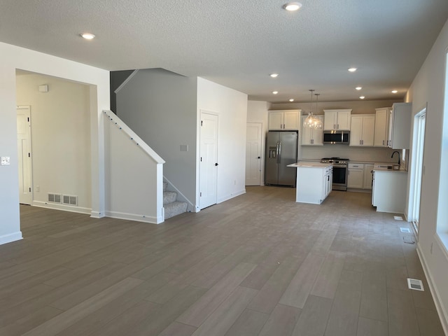 kitchen featuring appliances with stainless steel finishes, white cabinetry, hanging light fixtures, a center island, and light hardwood / wood-style floors