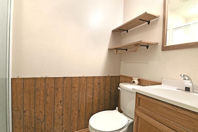 bathroom featuring toilet, vanity, and wood walls