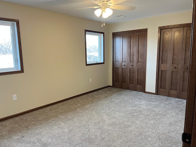 unfurnished bedroom featuring multiple windows, carpet flooring, visible vents, and multiple closets