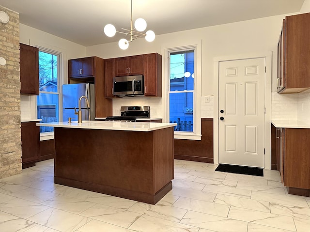 kitchen featuring an inviting chandelier, a center island with sink, hanging light fixtures, tasteful backsplash, and stainless steel appliances