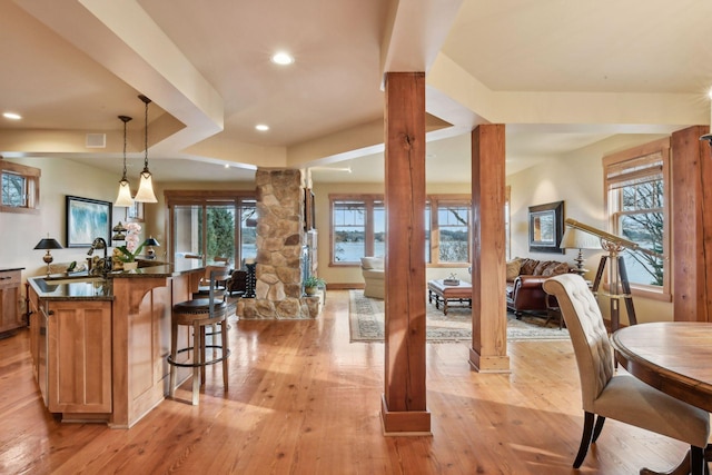 kitchen with sink, decorative columns, light wood-type flooring, and hanging light fixtures