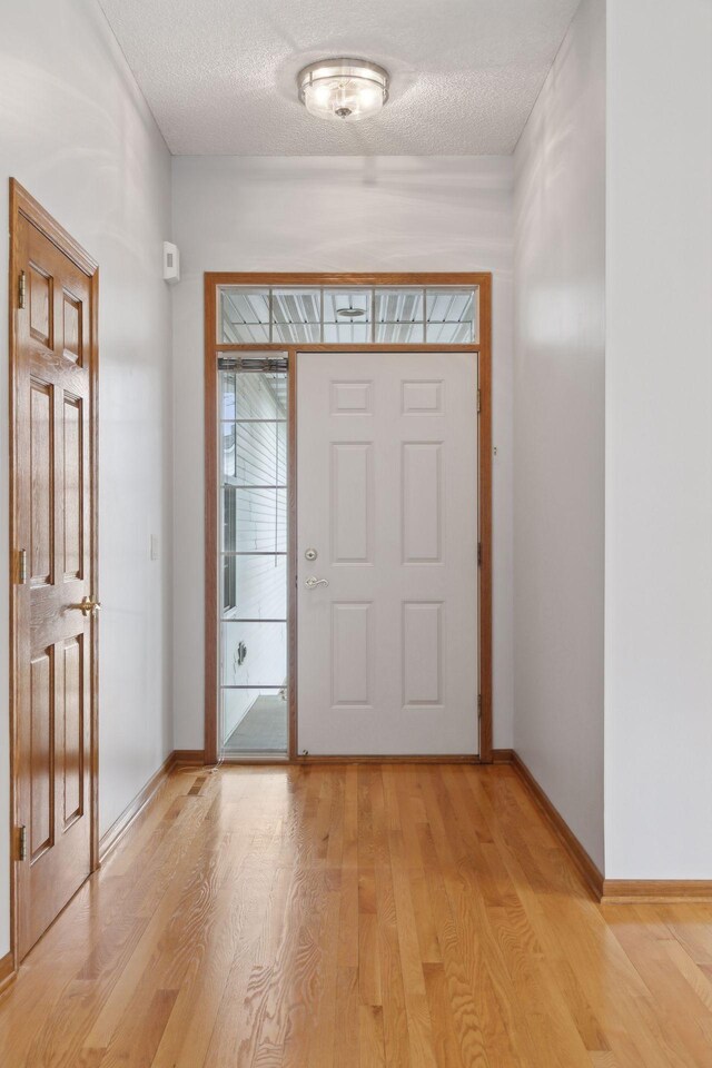 entryway with baseboards, light wood finished floors, and a textured ceiling