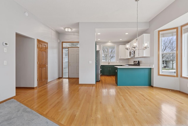 kitchen with light countertops, appliances with stainless steel finishes, light wood-style floors, an inviting chandelier, and white cabinetry