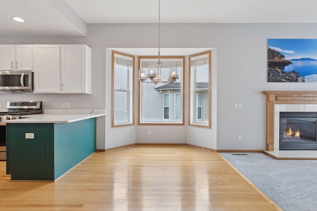 kitchen with an inviting chandelier, white cabinets, light wood-type flooring, and stainless steel appliances