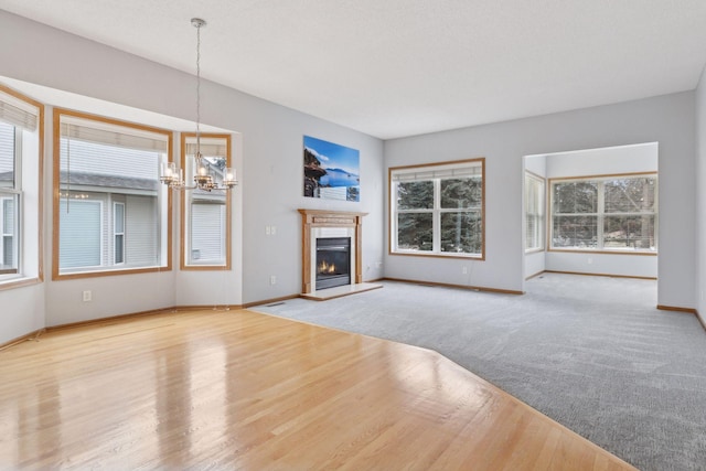 unfurnished living room with a chandelier, a glass covered fireplace, baseboards, and wood finished floors