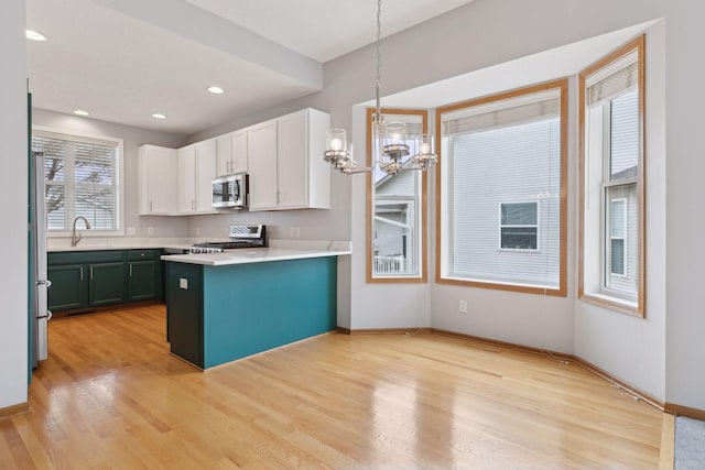 kitchen with light wood finished floors, a sink, appliances with stainless steel finishes, white cabinetry, and a notable chandelier