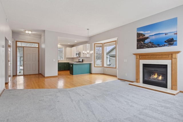 unfurnished living room with light carpet, a notable chandelier, a healthy amount of sunlight, and a glass covered fireplace