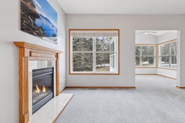 unfurnished living room with a glass covered fireplace, carpet flooring, a healthy amount of sunlight, and baseboards