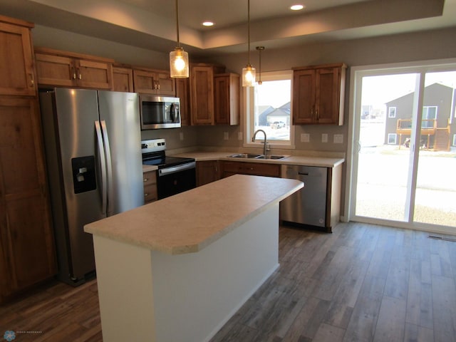 kitchen featuring a raised ceiling, sink, decorative light fixtures, a kitchen island, and stainless steel appliances