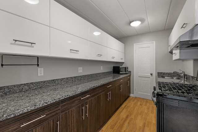 kitchen with black gas range, white cabinets, sink, light hardwood / wood-style flooring, and dark brown cabinetry