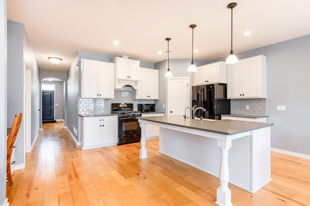 kitchen featuring a breakfast bar, a kitchen island with sink, black appliances, white cabinets, and decorative light fixtures