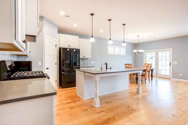 kitchen featuring black fridge with ice dispenser, range, a center island with sink, pendant lighting, and white cabinets