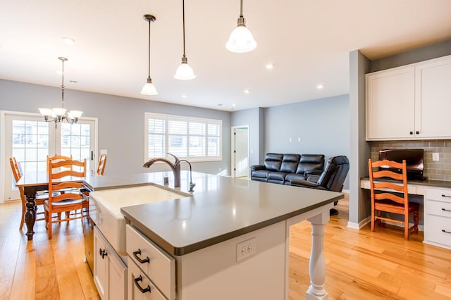 kitchen with hanging light fixtures, an island with sink, and white cabinets