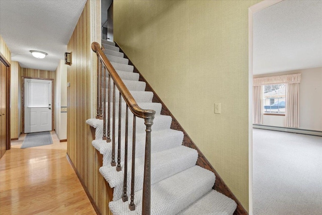 stairs featuring a textured ceiling, a baseboard heating unit, and hardwood / wood-style flooring