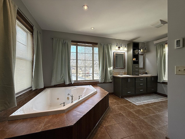 bathroom with double vanity, a tub with jets, a sink, and visible vents