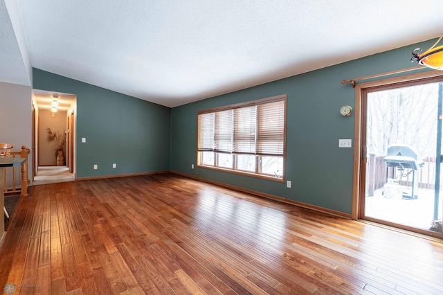 unfurnished living room with a textured ceiling, plenty of natural light, hardwood / wood-style floors, and vaulted ceiling