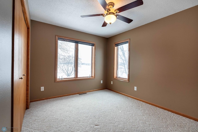 empty room featuring a textured ceiling, light colored carpet, and ceiling fan