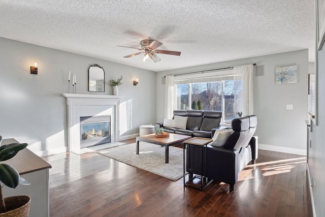 living room featuring ceiling fan, a textured ceiling, dark hardwood / wood-style flooring, and a tiled fireplace