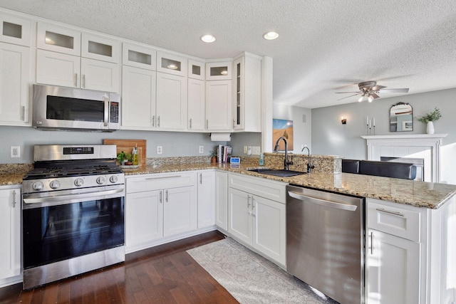 kitchen featuring kitchen peninsula, stainless steel appliances, white cabinets, light stone counters, and sink