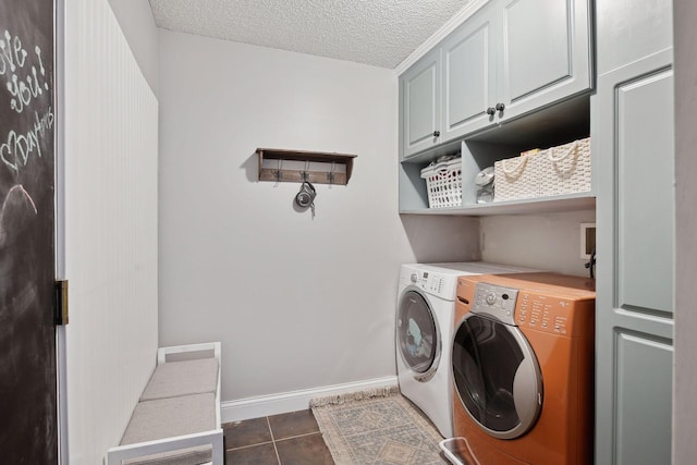 laundry area featuring a textured ceiling, dark tile patterned flooring, washing machine and clothes dryer, and cabinets