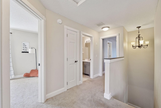 hallway with light colored carpet, a textured ceiling, and an inviting chandelier