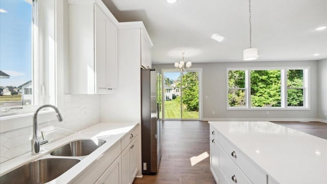 kitchen featuring stainless steel refrigerator, white cabinetry, sink, and hanging light fixtures