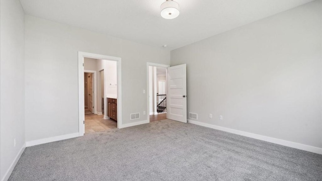 unfurnished bedroom featuring light colored carpet and ensuite bathroom