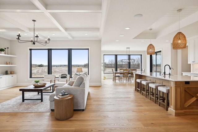 living room featuring beam ceiling, sink, coffered ceiling, light hardwood / wood-style flooring, and a chandelier