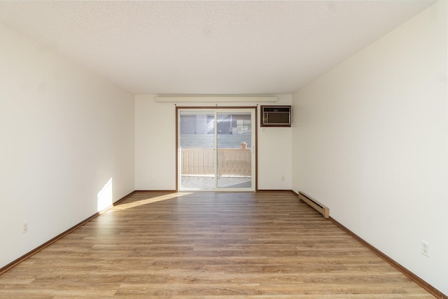 spare room with a textured ceiling, a baseboard radiator, an AC wall unit, and light hardwood / wood-style flooring