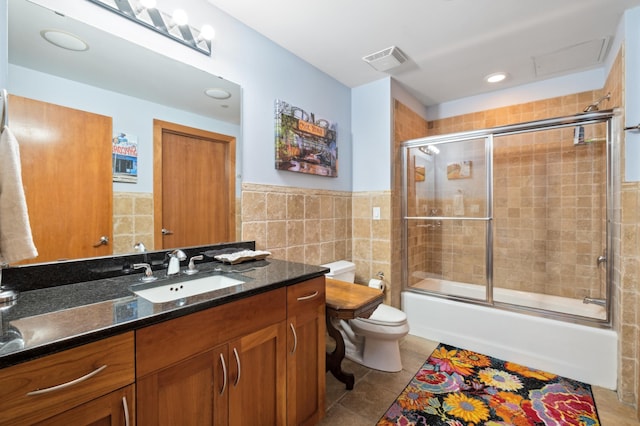 full bathroom with vanity, tile patterned floors, bath / shower combo with glass door, toilet, and tile walls