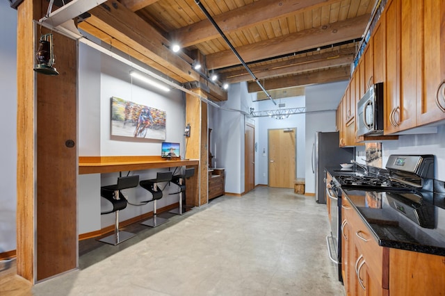 kitchen with finished concrete flooring, stainless steel appliances, brown cabinetry, and beamed ceiling