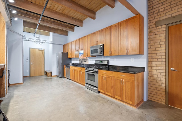 kitchen featuring brick wall, concrete floors, appliances with stainless steel finishes, beamed ceiling, and dark countertops