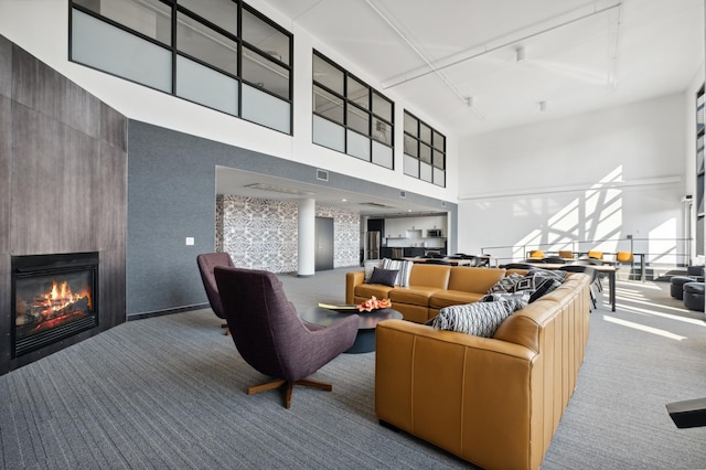 carpeted living room with a large fireplace, visible vents, rail lighting, and a towering ceiling