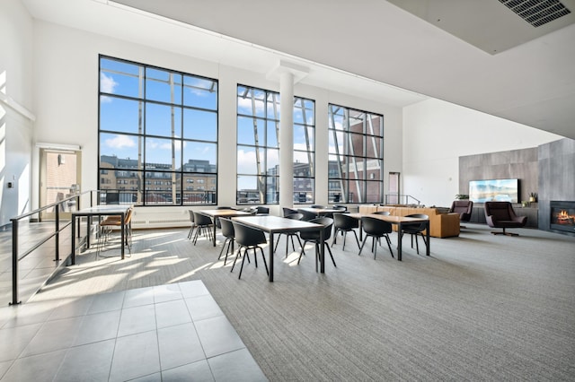 tiled dining room featuring a high ceiling, visible vents, a wealth of natural light, and a glass covered fireplace