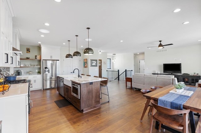 kitchen featuring stainless steel fridge, a center island with sink, decorative light fixtures, white cabinets, and hardwood / wood-style floors