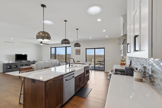 kitchen with dark brown cabinetry, stainless steel appliances, ceiling fan, pendant lighting, and an island with sink