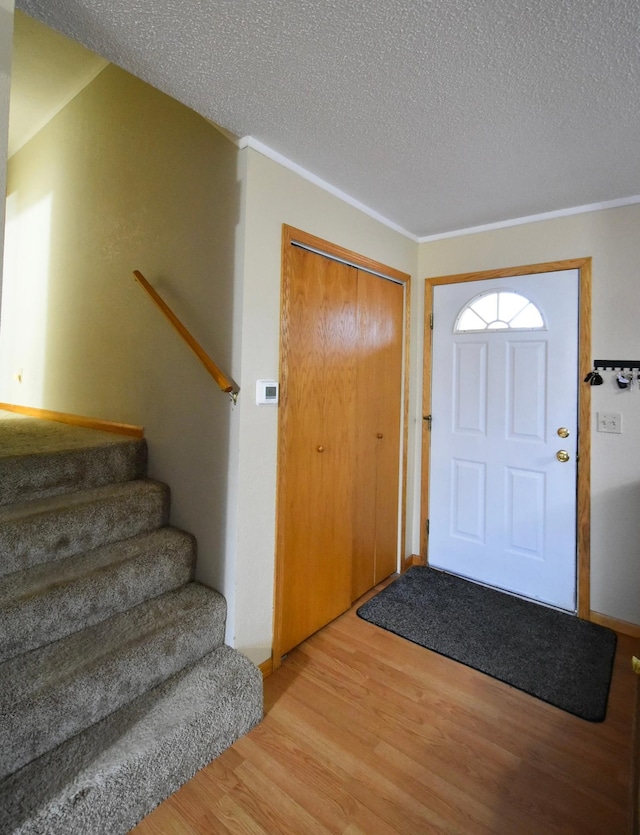 foyer entrance featuring a textured ceiling, light wood-type flooring, and crown molding