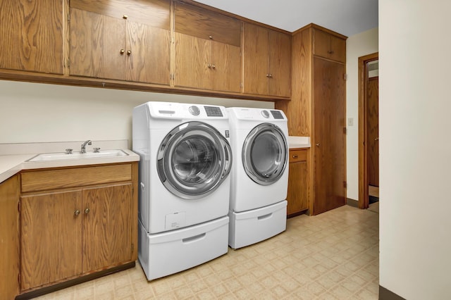 clothes washing area with sink, washing machine and dryer, and cabinets