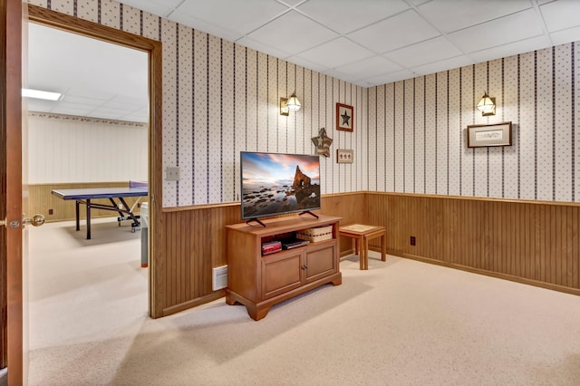 carpeted living room featuring a drop ceiling and wood walls