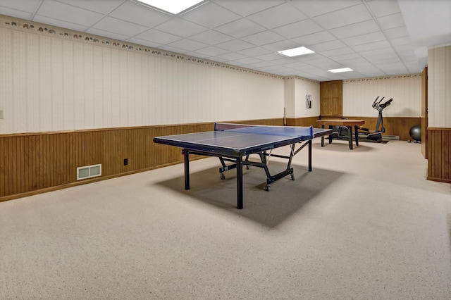 recreation room featuring carpet floors, a drop ceiling, and wooden walls