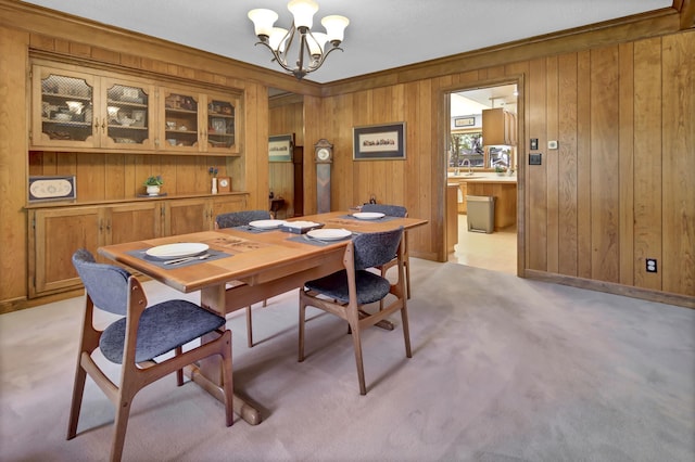 carpeted dining room with a notable chandelier, crown molding, wooden walls, and sink