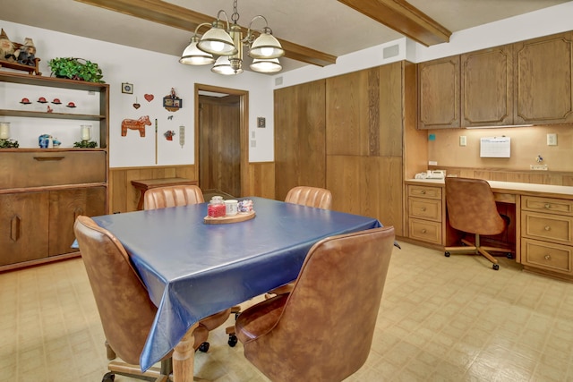 dining space featuring a chandelier, beam ceiling, built in desk, and wood walls