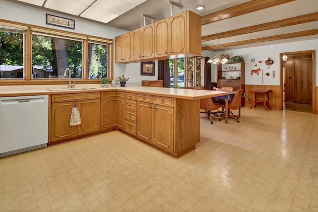 kitchen with wood walls, sink, hanging light fixtures, white dishwasher, and kitchen peninsula