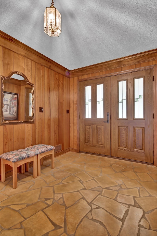 entryway featuring an inviting chandelier, a textured ceiling, and wood walls