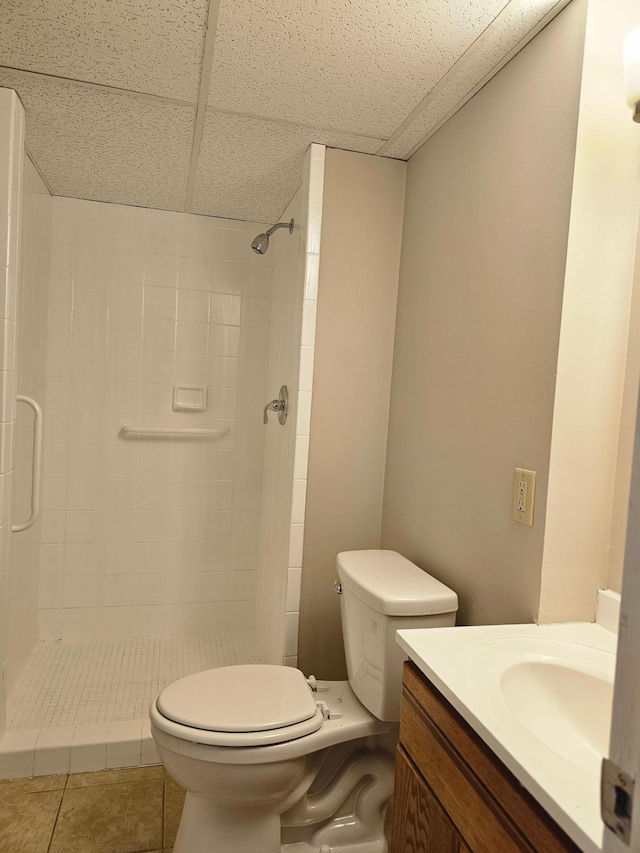 bathroom with tile patterned floors, a paneled ceiling, tiled shower, and toilet