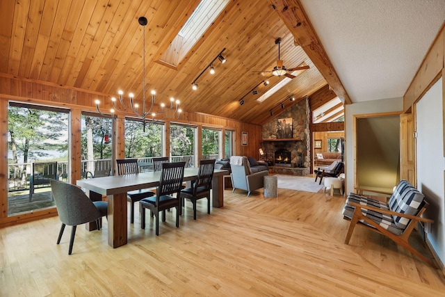 dining room with wood walls, a skylight, ceiling fan, light wood-type flooring, and a fireplace