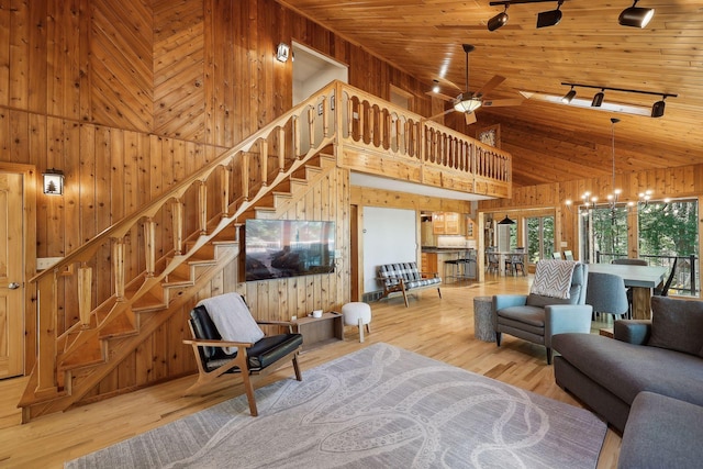 living room featuring a high ceiling, ceiling fan with notable chandelier, light hardwood / wood-style floors, and wood walls