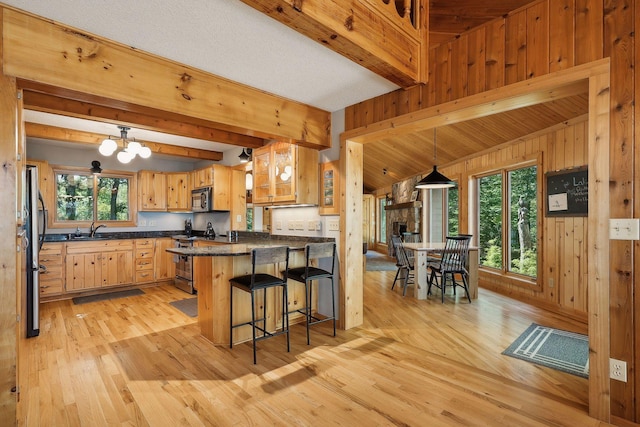 kitchen featuring a breakfast bar, wood walls, sink, light hardwood / wood-style flooring, and appliances with stainless steel finishes